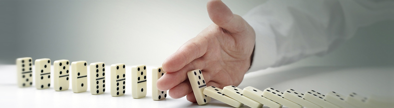 Eine Hand stoppt fallende Dominosteine